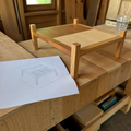 Printed woodworking plan with dimension drawing beside a solid oak coffee table on a walnut workbench