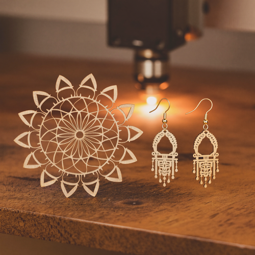 Laser-cut wooden earrings and layered mandala beside a desktop laser cutter