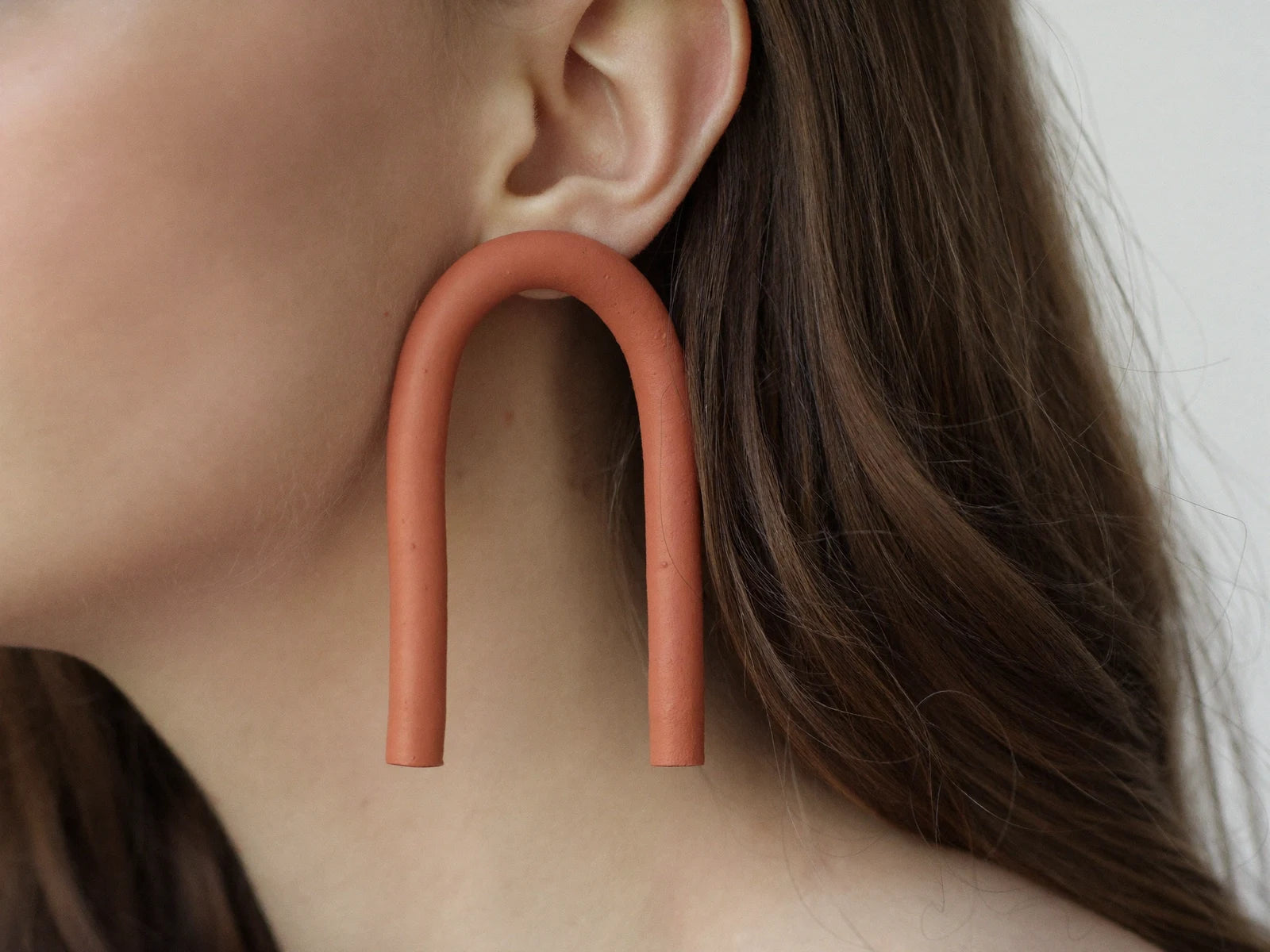 A terracotta clay arch earring worn on an ear.