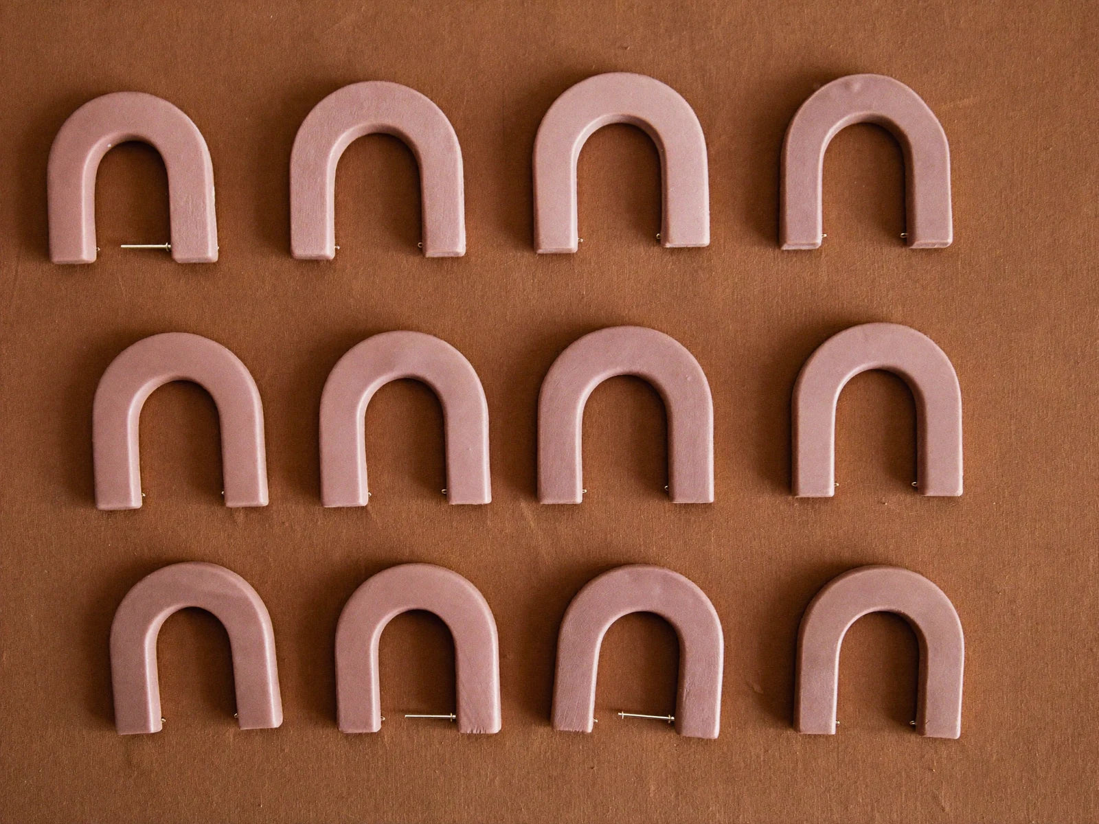 Twelve identical pairs of clay earrings in perfect rows, showing flawless batch consistency